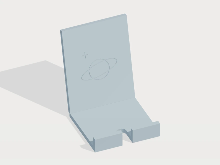 3D model preview of a tilted phone stand with a planet-and-orbit engraving, retaining lip and charging cutout